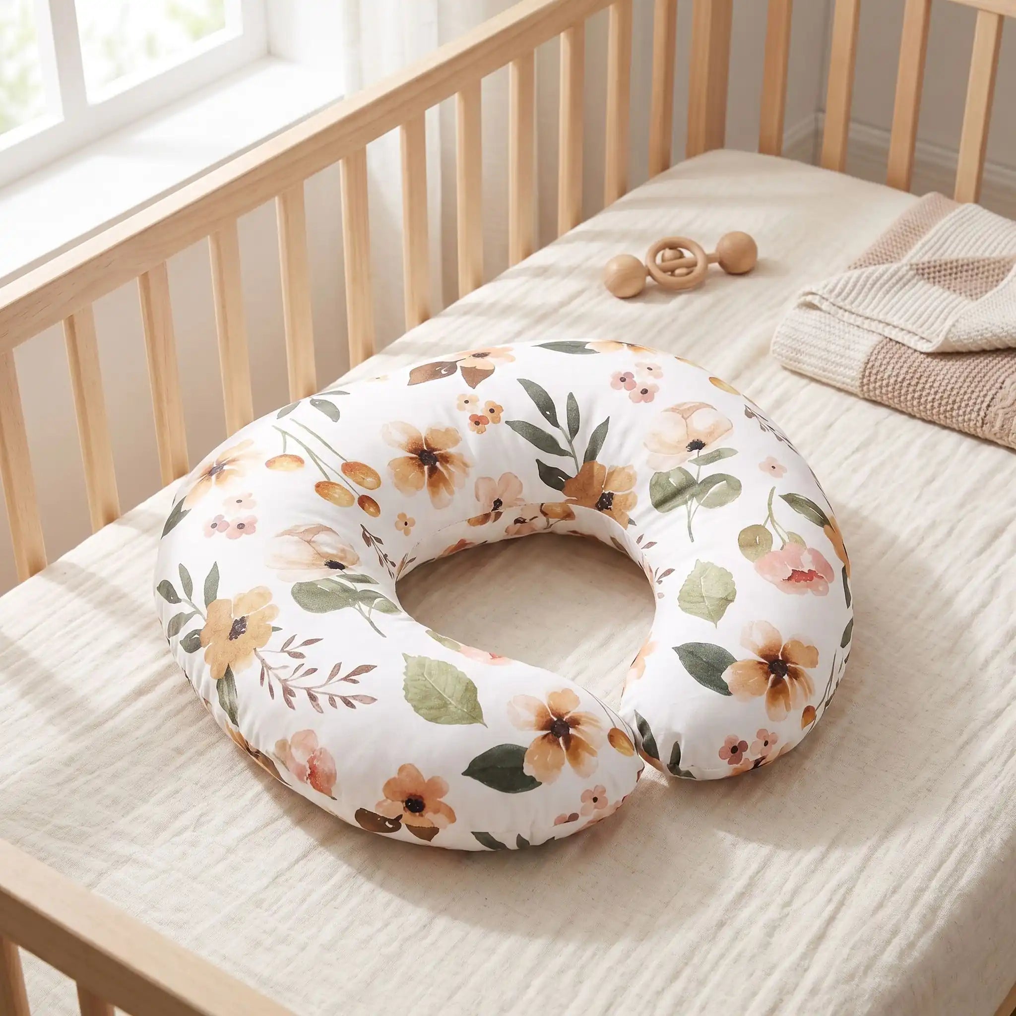Coussin allaitement en forme de U floral posé seul sur un lit de bébé en bois